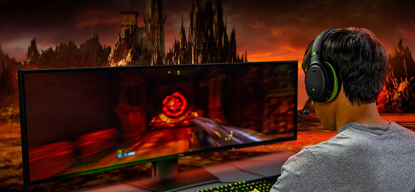 man wearing Penrose X headphones in front of widescreen gaming display